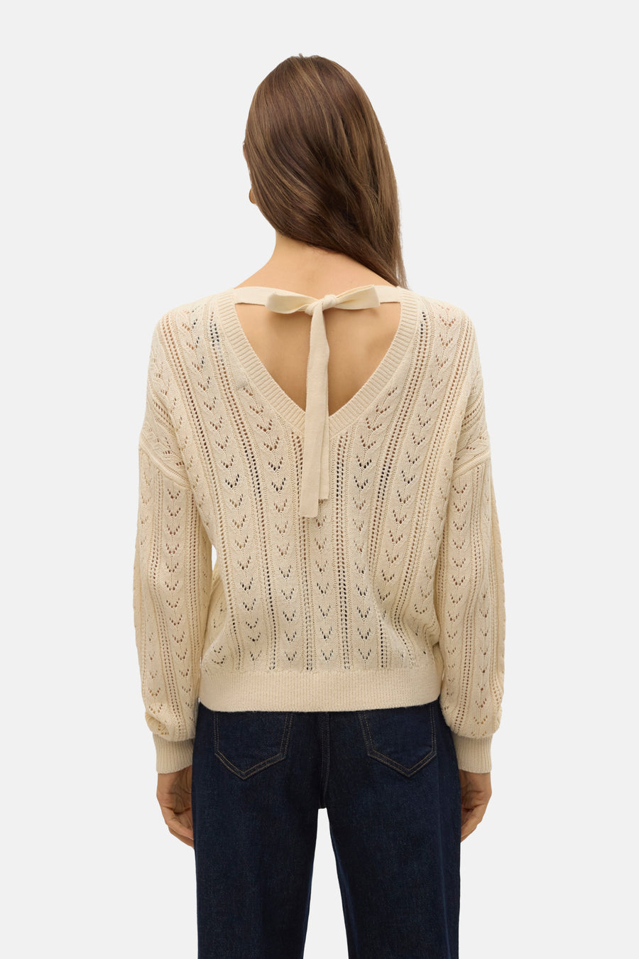 Vrouw van achter in gebreide trui met strik op de rug, blauwe jeans.