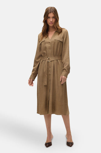 Vrouw in bruine linnen jurk met ceintuur en bruine schoenen, staand.