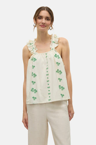 Blouse écru sans manches de VERO MODA®, avec des motifs de fleurs vertes et des volants sur les épaules, associée à une jupe beige et des bottines vertes.