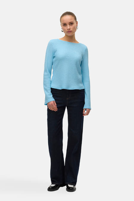 T-shirt bleu à manches longues de VERO MODA avec une texture à carreaux, associé à des jeans foncés et des boucles d'oreilles argentées.