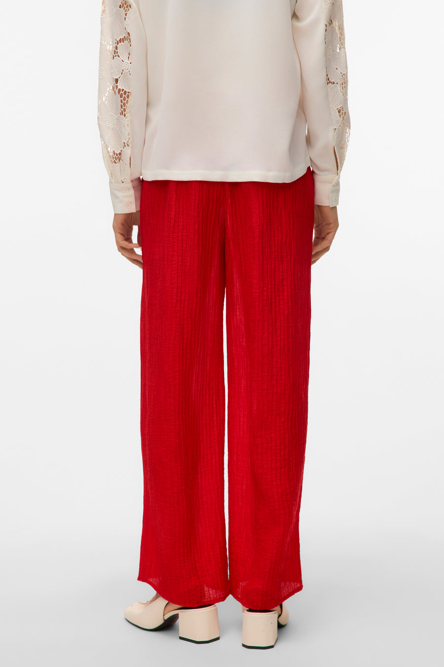 Achterkant van een vrouw met witte blouse en rode plissé broek.