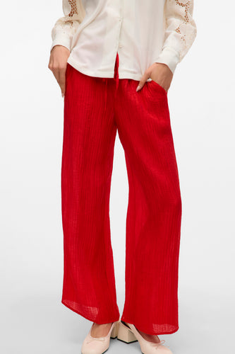 Rode, wijde broek van kreukelstof met beige schoenen en witte blouse.