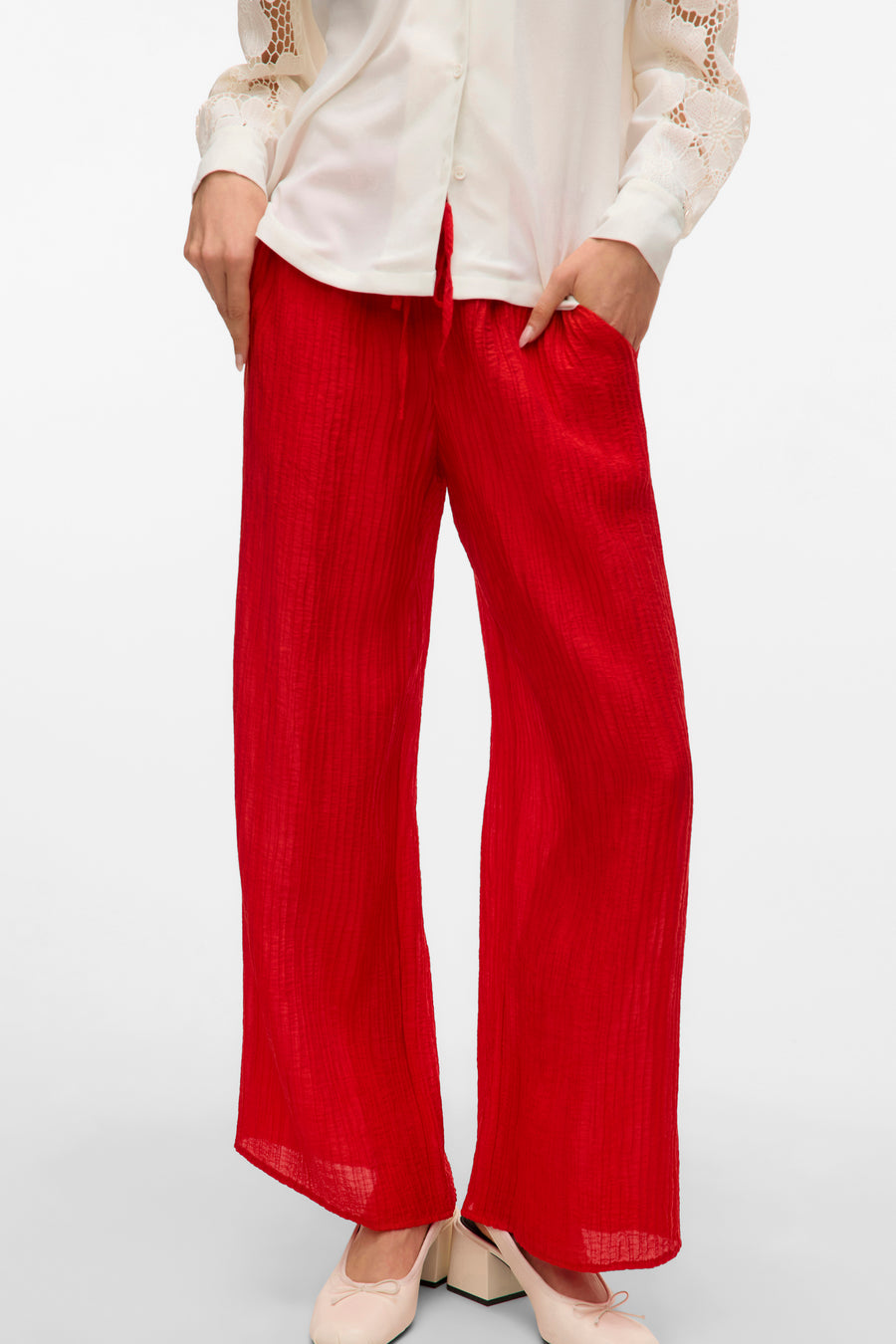 Rode, wijde broek van kreukelstof met beige schoenen en witte blouse.