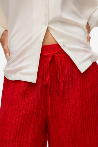 Close-up van een wit blouse en rode crêpe broek.
