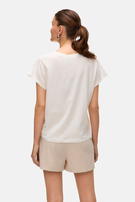 T-shirt blanc à manches courtes de VERO MODA, vu de dos, avec des shorts beige et des boucles d'oreilles argentées.