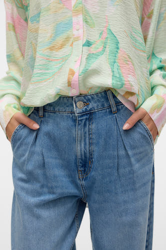 Jean spécial fit en denim bleu de VERO MODA, avec plis et poches, associé à une blouse à imprimé abstrait.
