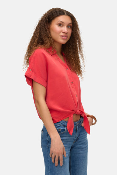 T-shirt rouge à manches courtes de VERO MODA, boutonné devant, associé à des jeans bleus et un unmband en bois.