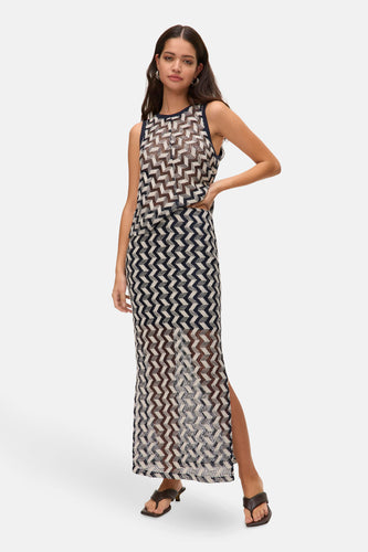 Vrouw in lange jurk met zigzagpatroon en bruine slippers.
