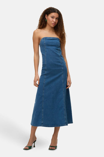 Een vrouw draagt een strapless, blauwe denim jurk en groene schoenen op een witte achtergrond.