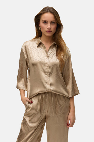 Chemise beige à manches courtes de VERO MODA, avec un motif ondulé subtil, portée avec un pantalon coordonné et des chaussures vertes.
