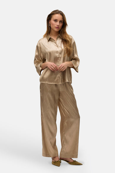 Beige hemd met korte mouwen van VERO MODA, met een subtiel golvend patroon, gedragen met een bijpassende broek en groene schoenen.
