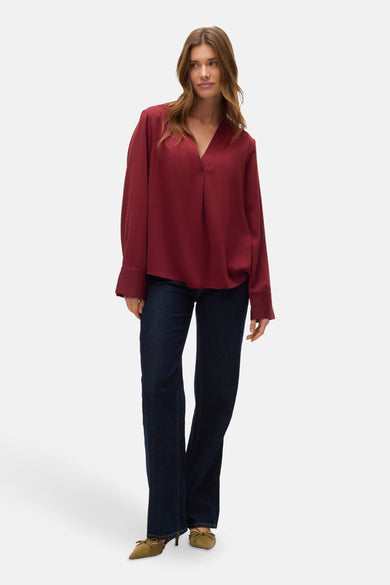 Blouse rouge à longues manches de VERO MODA, associée à des jeans foncés et des escarpins vert olive.