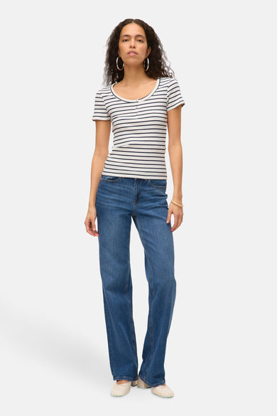 T-shirt rayé blanc à manches courtes de VERO MODA, avec détail de bouton et associé à des jeans larges et des chaussures.