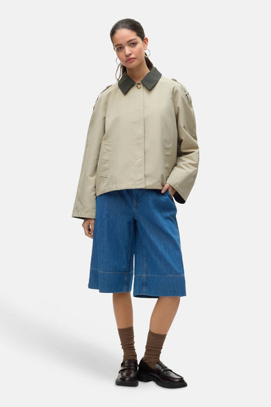 Ecru manteau court de VERO MODA, avec un col sombre, associé à un pantalon de denim large et des loafers bruns.