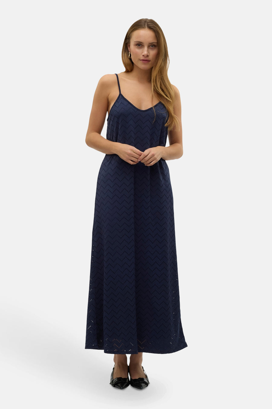 Een vrouw in een lange, blauwe, mouwloze jurk met een patroon staat voor een witte achtergrond.