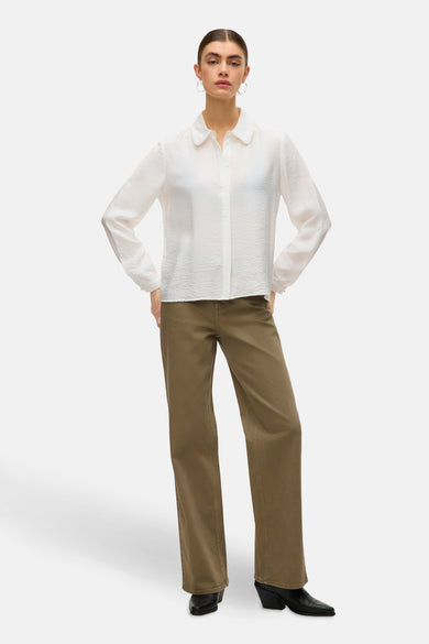 Blouse blanche à manches longues de VERO MODA, avec col et texture visible, associée à un pantalon vert et des bottes.