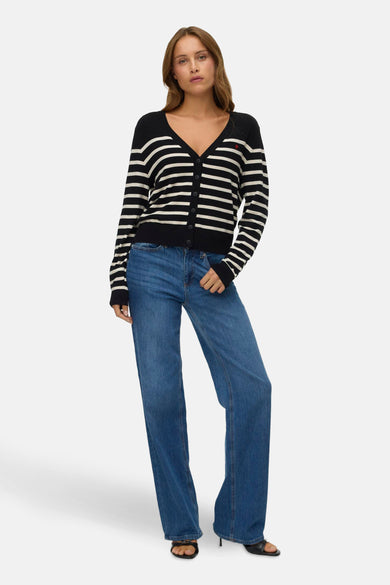 Gilet noir de Vero Moda avec des rayures blanches, porté sur un jean bleu à déchirures.