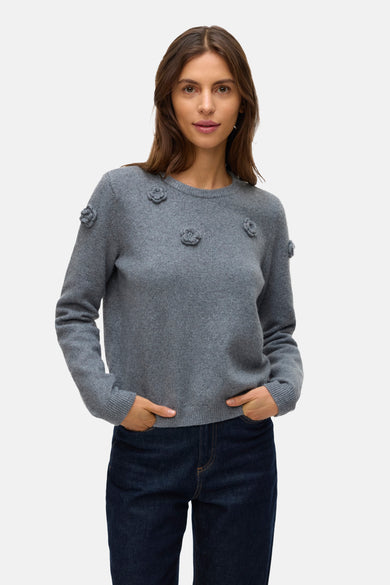 Pull rond col en gris VERO MODA® avec des détails floraux sur les épaules et la poitrine, associé à un jeans foncé.