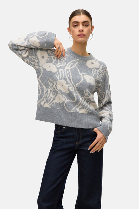 Sweat-shirt gris à col rond de VERO MODA® avec motif floral, associé à des jeans foncés et des boucles d'oreilles argentées.