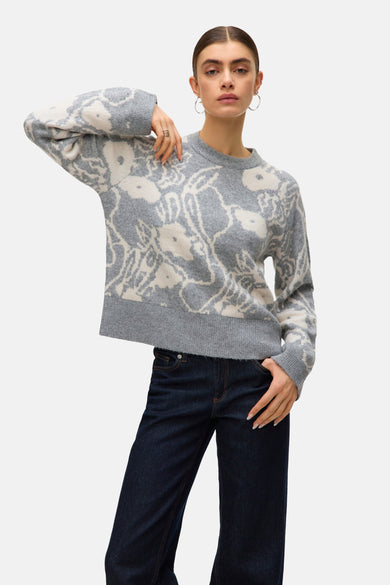Sweat-shirt gris à col rond de VERO MODA® avec motif floral, associé à des jeans foncés et des boucles d'oreilles argentées.