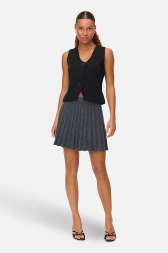 Jupe grise courte de VERO MODA, avec des plis et portée avec une chemise noire et des sandales.