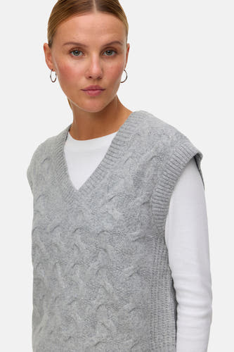 Veste grise tricotée de VERO MODA, avec un col en V, portée sur une chemise blanche, avec des boucles d'oreilles argentées.