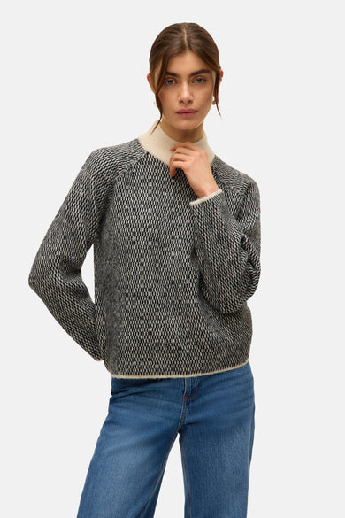 Pull noir avec col rond de VERO MODA, avec un motif graphique, associé à des jeans bleus et des chaussures marrons.