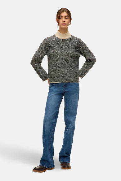 Zwarte trui met ronde hals van VERO MODA®, met een grafisch patroon, gecombineerd met blauwe jeans en bruine schoenen.
