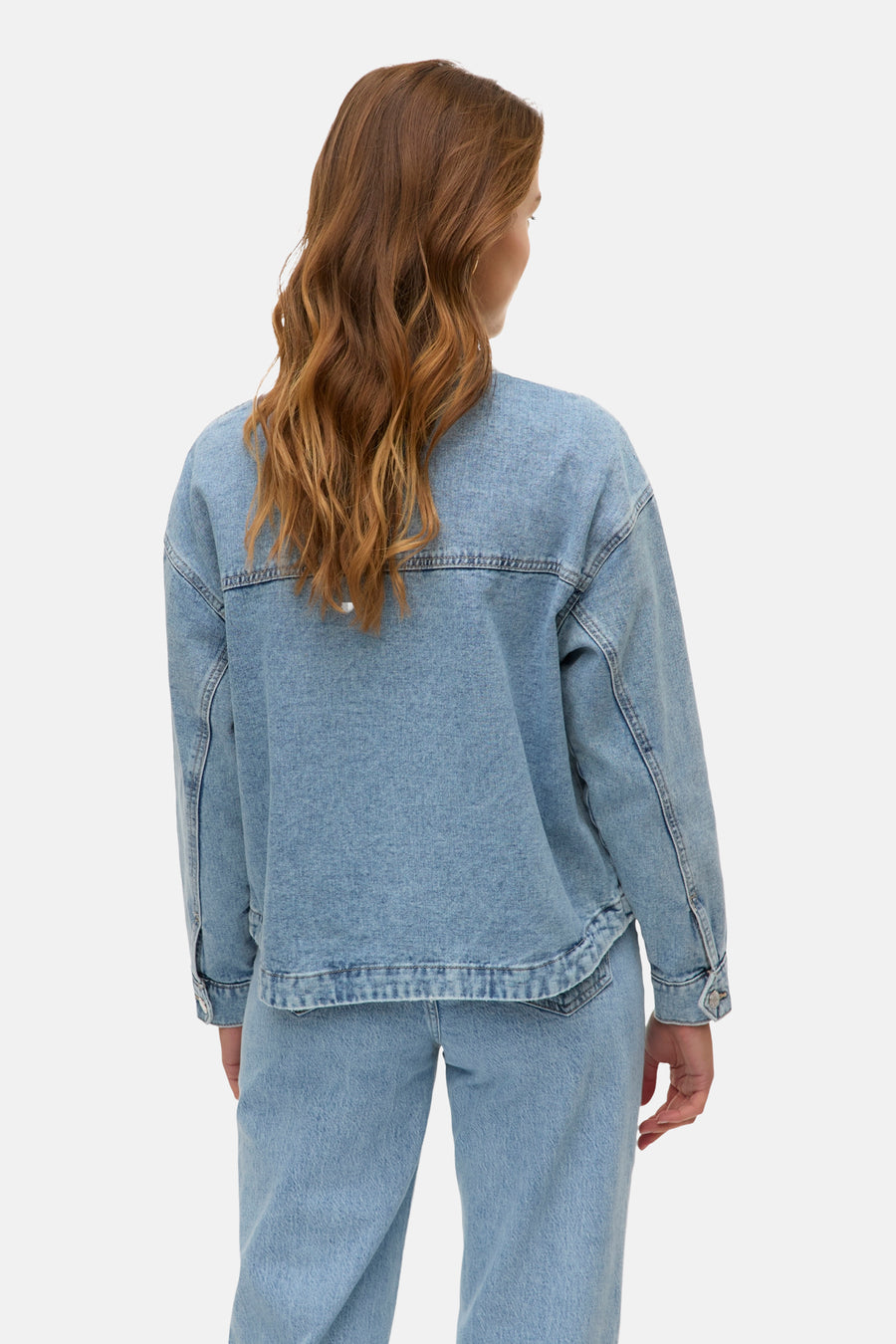Lichtblauwe denim jas van Vero Moda, gezien van achteren, met golvend bruin haar.
