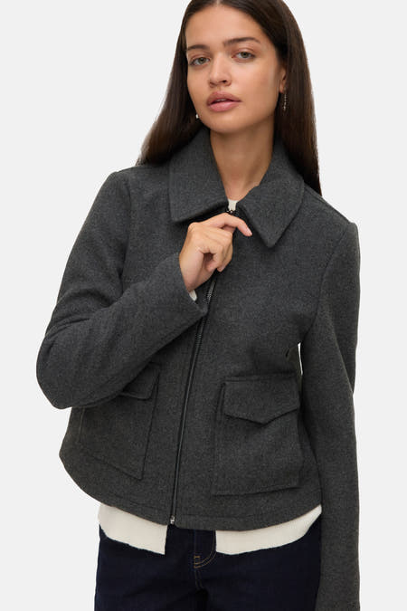 Manteau gris de VERO MODA avec fermeture éclair, longueur courte et poches brodées.