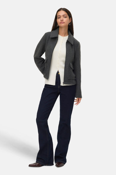 Manteau court gris de VERO MODA®, avec des manches longues, porté sur une chemise blanche et un jeans foncé.