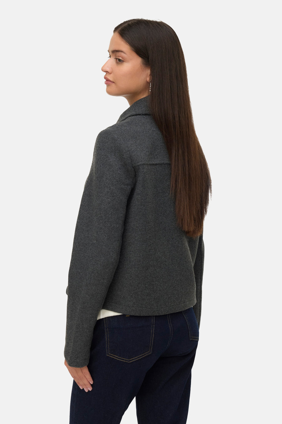 Vrouw met grijs jasje en blauwe jeans.