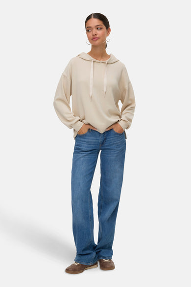 Sweater écru de VERO MODA avec capuche, porté avec des jeans bleus et des chaussures marrons.