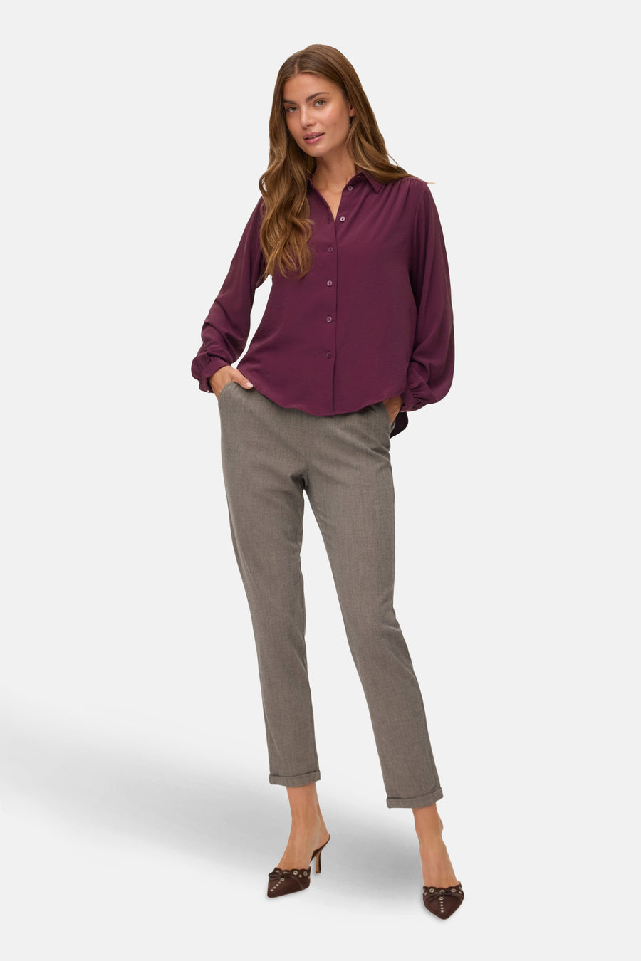 Vrouw met bordeauxrode blouse, grijze broek, hakken, staand.