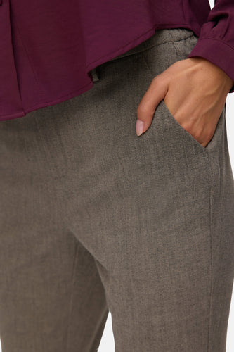 Bruine pantalon met hand in zak en bordeauxrode blouse.