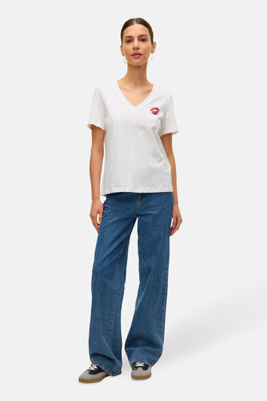 T-shirt blanc à manches courtes de VERO MODA® avec imprimé de lèvres rouges, associé à des jeans bleus.