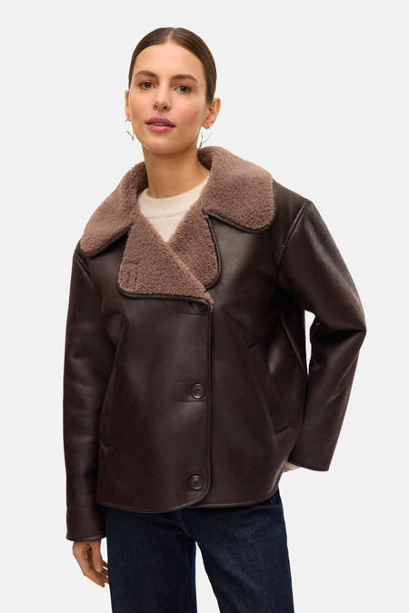 Manteau court brun de Vero Moda, avec col en fourrure et fermeture à boutons, porté avec un pull blanc et des jeans bleu marine.