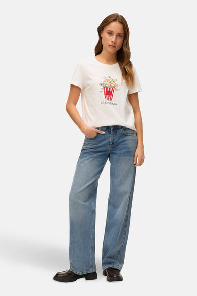 T-shirt blanc à manches courtes de VERO MODA, avec imprimé popcorn et jeans larges et chaussures noires.
