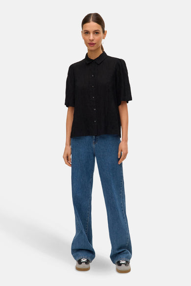 Chemise noire à manches courtes de VERO MODA, avec texture et portée avec des jeans bleus et des chaussures grises.