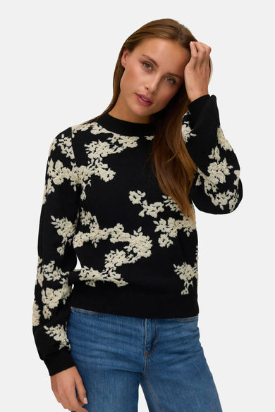Pull noir avec col rond de VERO MODA, avec un motif floral sur toute la chemise, associé à un jean bleu.