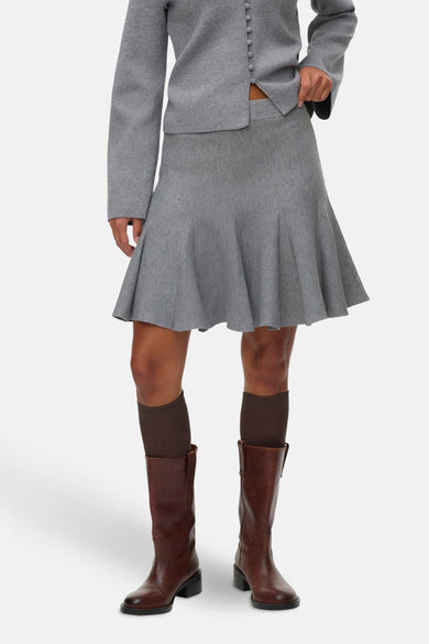 Jupe grise courte de VERO MODA, avec des plis et associée à des bottes brunes et des chaussettes.