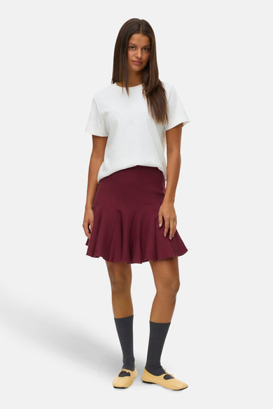 Jupe courte bordeaux de VERO MODA®, avec une coupe évasée et portée avec un t-shirt blanc et des chaussures Mary Jane.
