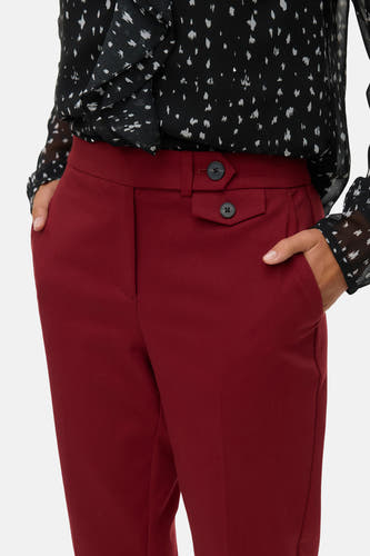 Pantalon rouge de VERO MODA, avec des boutons décoratifs et des poches, associé à une blouse imprimée noir et blanc.