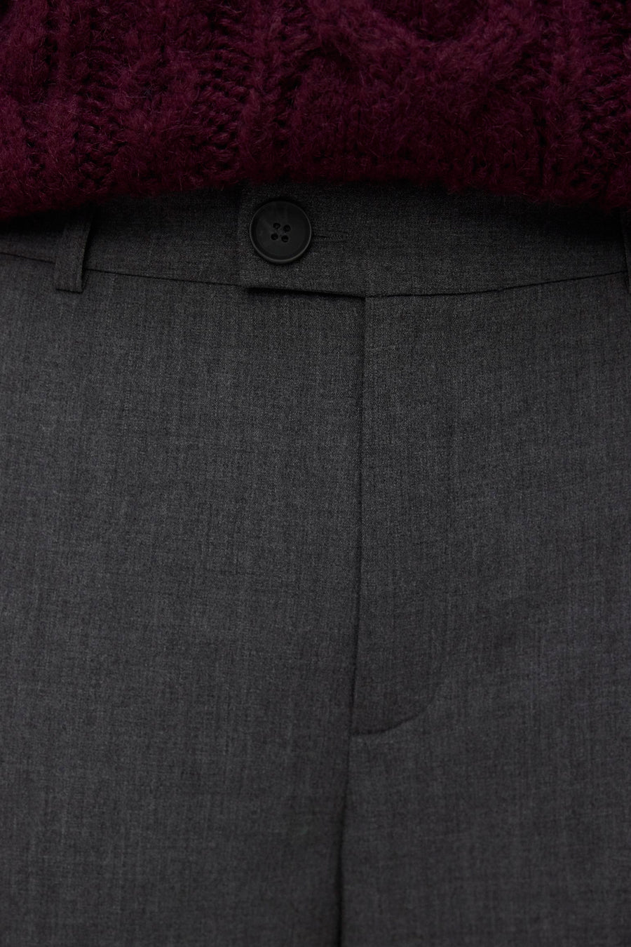 Grijze pantalon met knoop en paarse trui.
