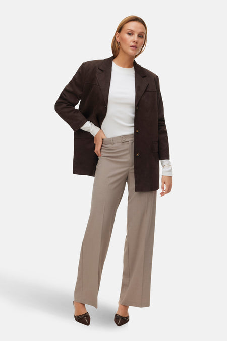 Vrouw in bruin pak met witte top en bruine schoenen, staand.