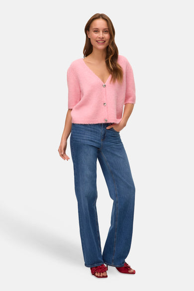 Gilet rose de VERO MODA, porté avec un jean à jambes larges et des chaussures rouges à détails floraux.