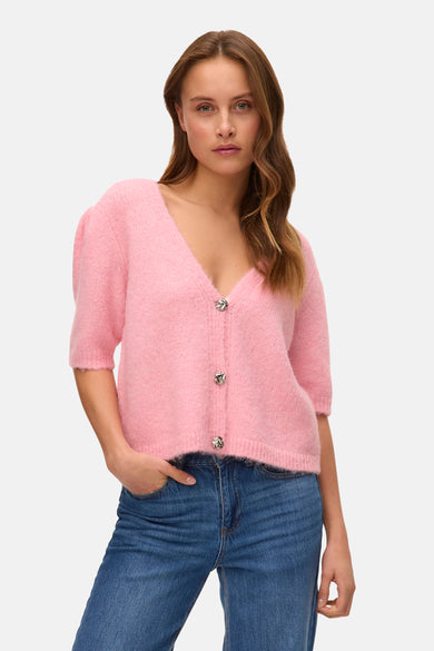 Gilet rose de VERO MODA avec des manches courtes et des boutons décoratifs, porté sur un jean bleu.