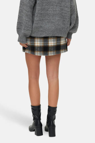 Jupe courte multicolore de VERO MODA avec un motif à carreaux, associée à une chemise grise et des bottes noires.