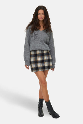 Jupe courte multicolore de Vero Moda, avec un motif à carreaux, associée à une chemise grise et des bottes noires.