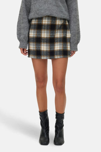 Jupe courte multicolore de VERO MODA, avec un motif à carreaux et associée à des bottes noires et une chemise grise.